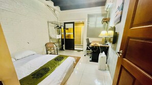 Habitación de hotel con cama, escritorio, silla y baño visible a través de una puerta abierta.
