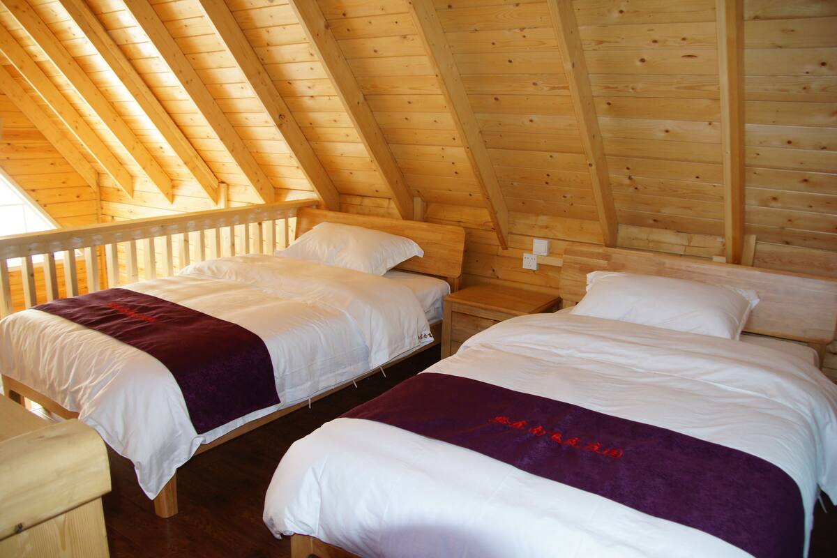A room with two beds, wooden walls, and a sloped ceiling.