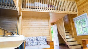 Interior de una cabaña de madera con habitación en el altillo, una escalera y vistas al exterior.