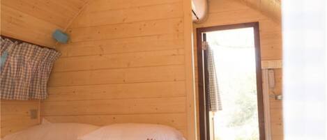 A wooden cabin room with a bed, a window, and a door.