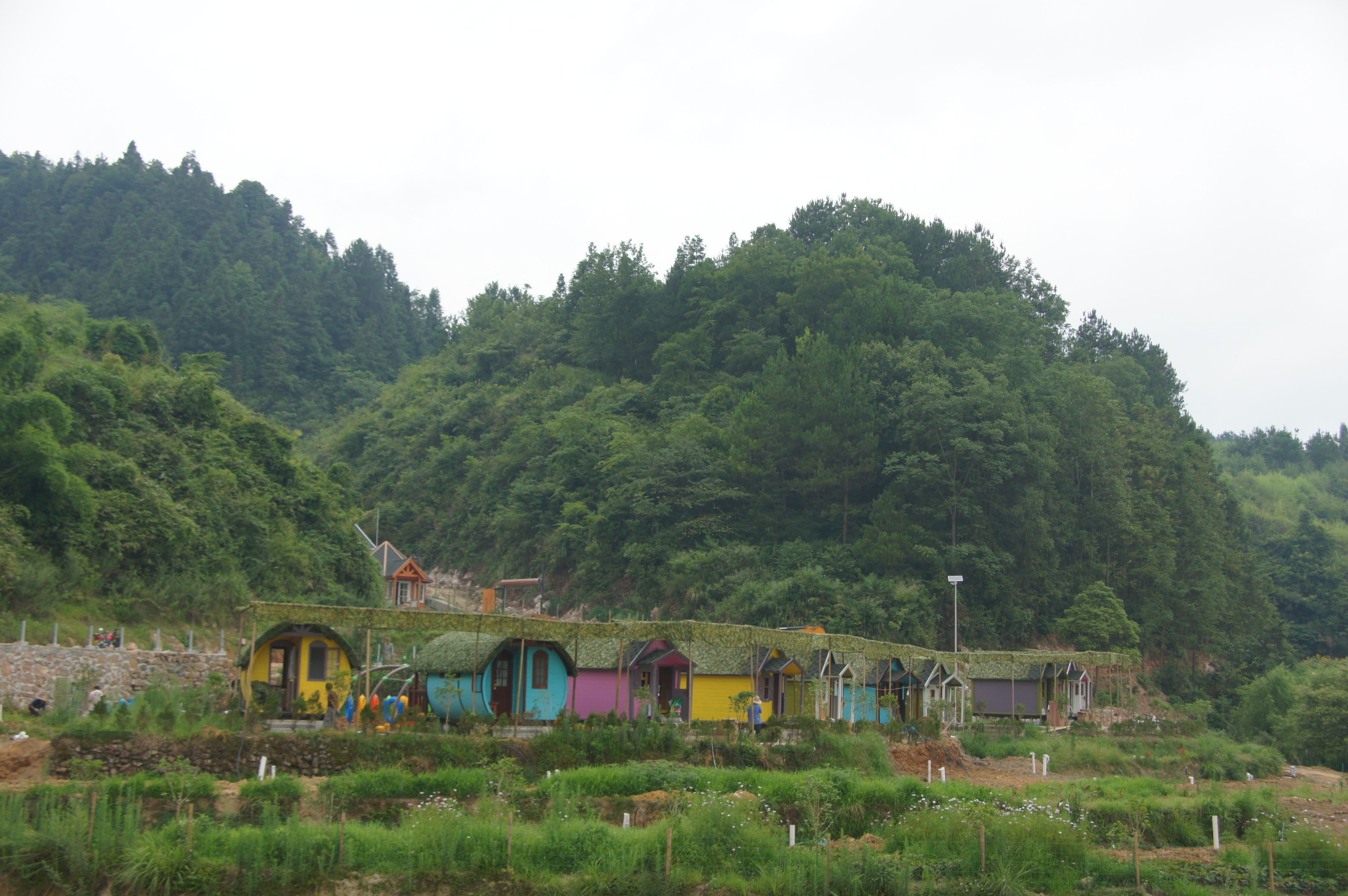 A row of colorful, rustic cabins with thatched roofs, surrounded by lush greenery and hills.