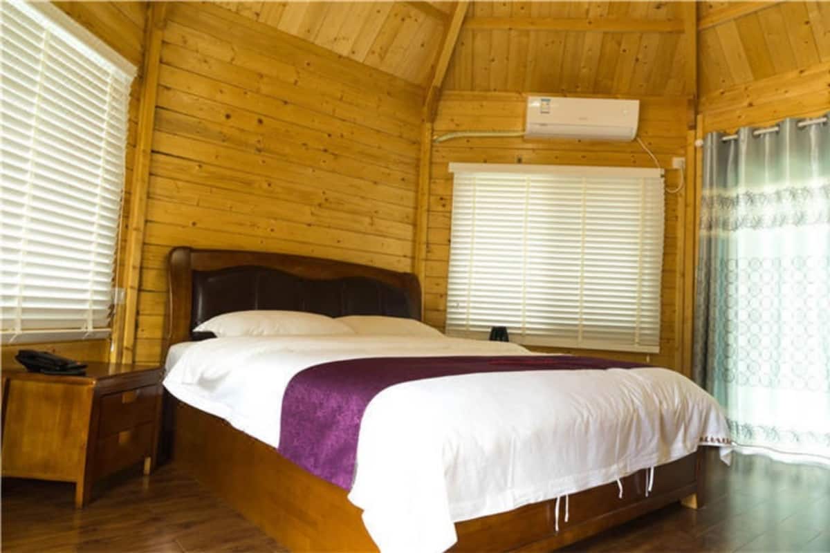 A wooden-paneled room with a bed, a nightstand, a window with blinds, and an air conditioning unit.