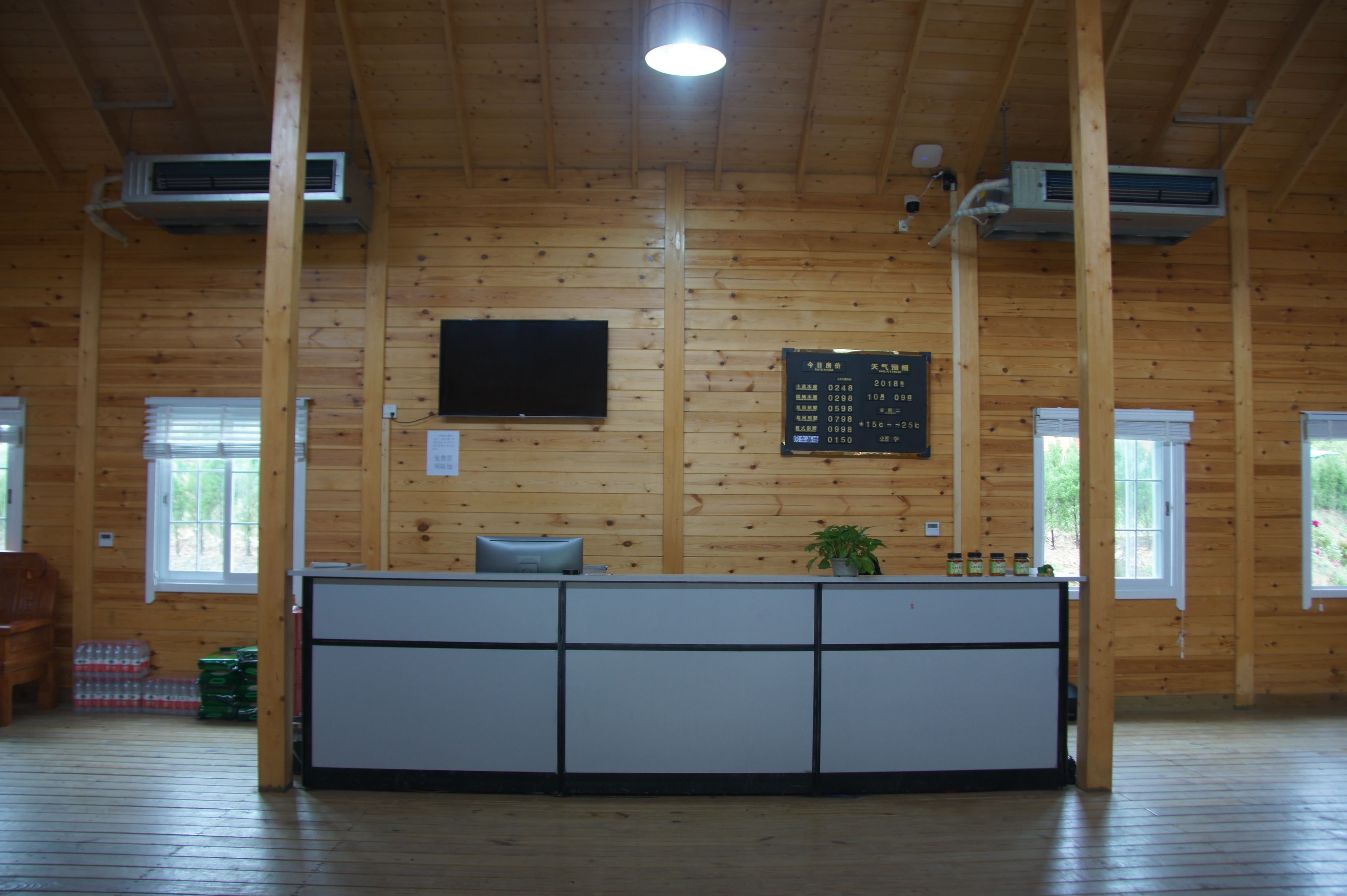Un área de recepción con interior de madera, un mostrador de recepción, un televisor y una pizarra de anuncios.
