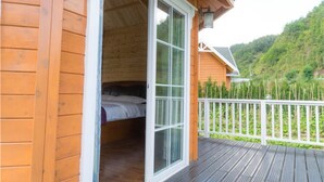Una cabaña de madera con un dormitorio que tiene una cama, puerta corrediza de vidrio y una terraza con barandilla blanca.