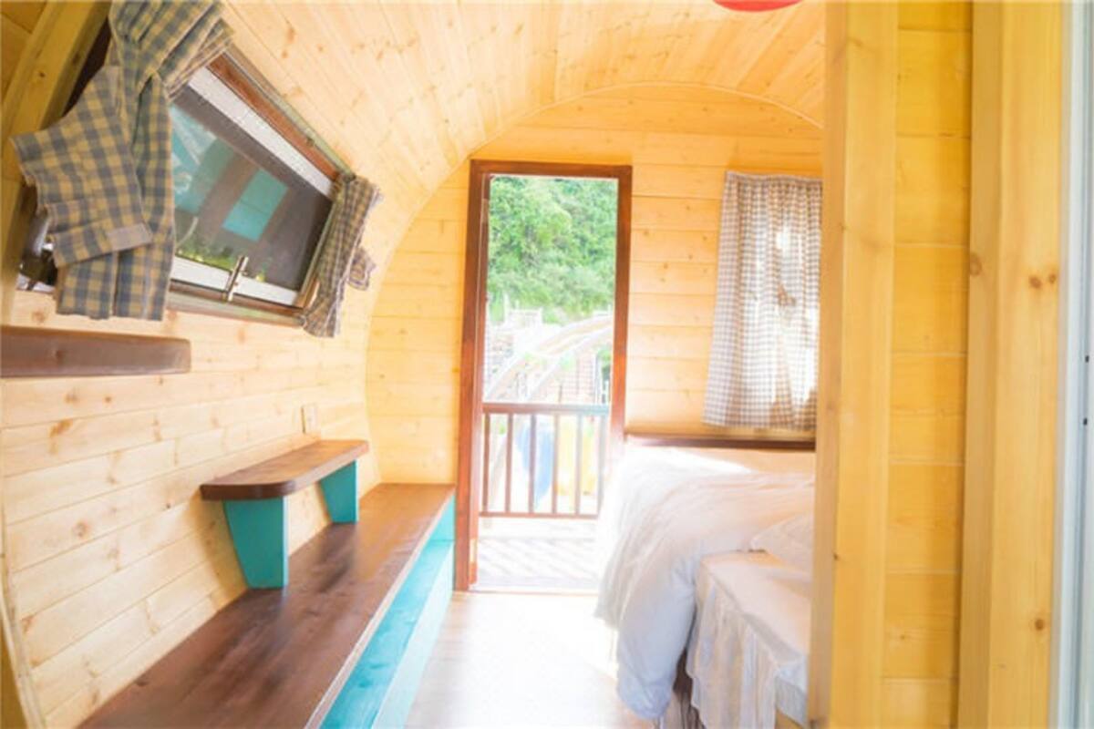 A wooden cabin with a bed, a bench, a window, and a door leading outside.