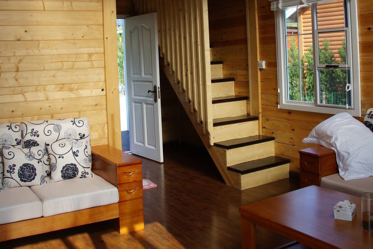 A wooden interior with a loft bedroom, a staircase, a sofa, a table, and a window with a view.