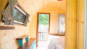 Una habitación tipo cabaña de madera con una cama, un banco y una ventana con cortinas.