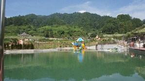 Un cuerpo de agua tranquilo con una estructura de juegos, rodeado de exuberante vegetación y colinas.