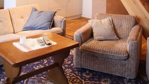 Una sala de estar acogedora con sofá, sillones, una mesita de centro y una escalera que sube a un nivel superior.