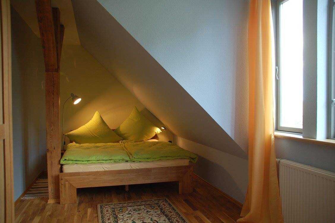 A bedroom with a sloped ceiling, a wooden bed, and a window with curtains.