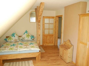 A bedroom with a sloped ceiling, a wooden bed with floral bedding, a wooden wardrobe, and a door leading to another room. - Apartment Dandelion - I know a house on the forest ... (Teterow)