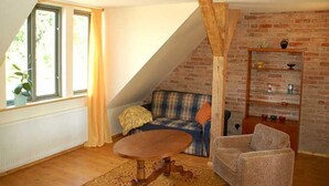 Un salón acogedor con techo inclinado, un sofá, un sillón, una mesita y una pared de ladrillo con estanterías.