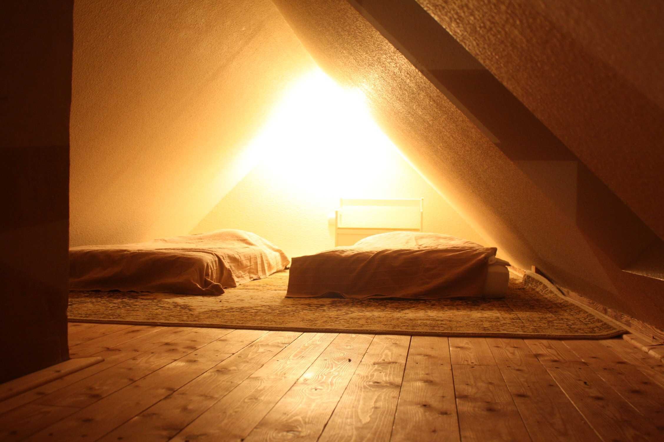 A small, dimly lit attic bedroom with two beds and a single light source.