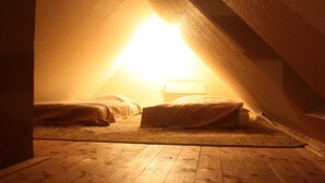 Un pequeño dormitorio bajo las tejas, con poca luz, que tiene dos camas y una única fuente de iluminación.