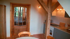 Una cocina rústica con vigas de madera, un puerta de madera, una mesa de comedor y un respaldo de azulejos.