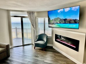 Una sala de estar con un televisor de pantalla plana grande, un sillón cómodo, una chimenea y un balcón con vistas al océano.