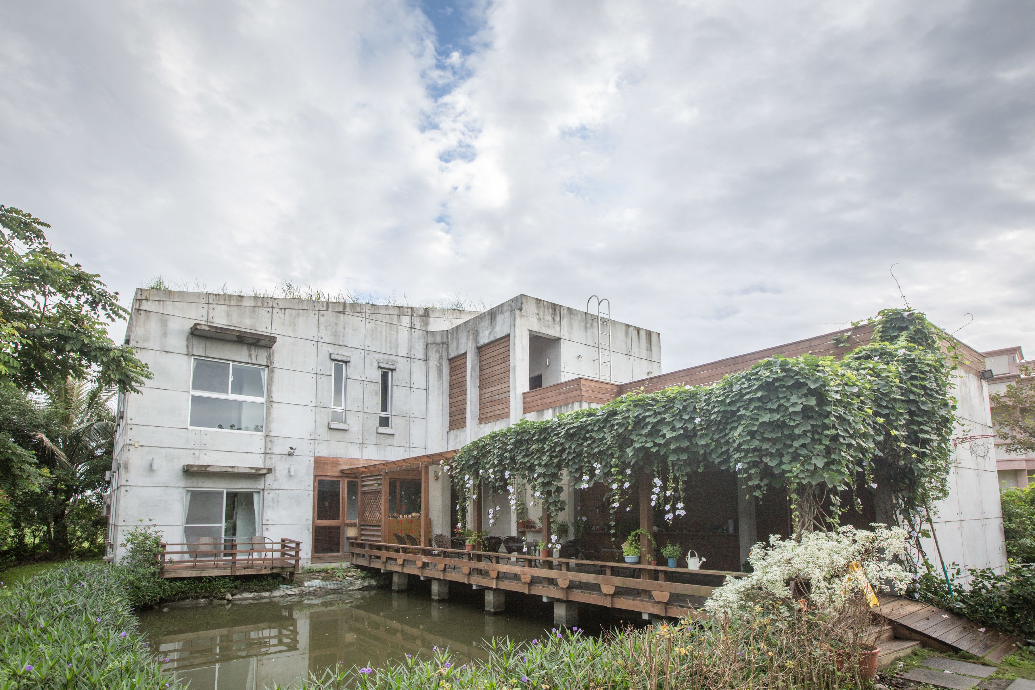 A modern building with a garden, a bridge, and a pond.