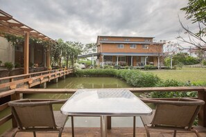 A wooden deck with a table and chairs overlooking a pond and a building with a garden. - Just Like Villa (Ji'an)