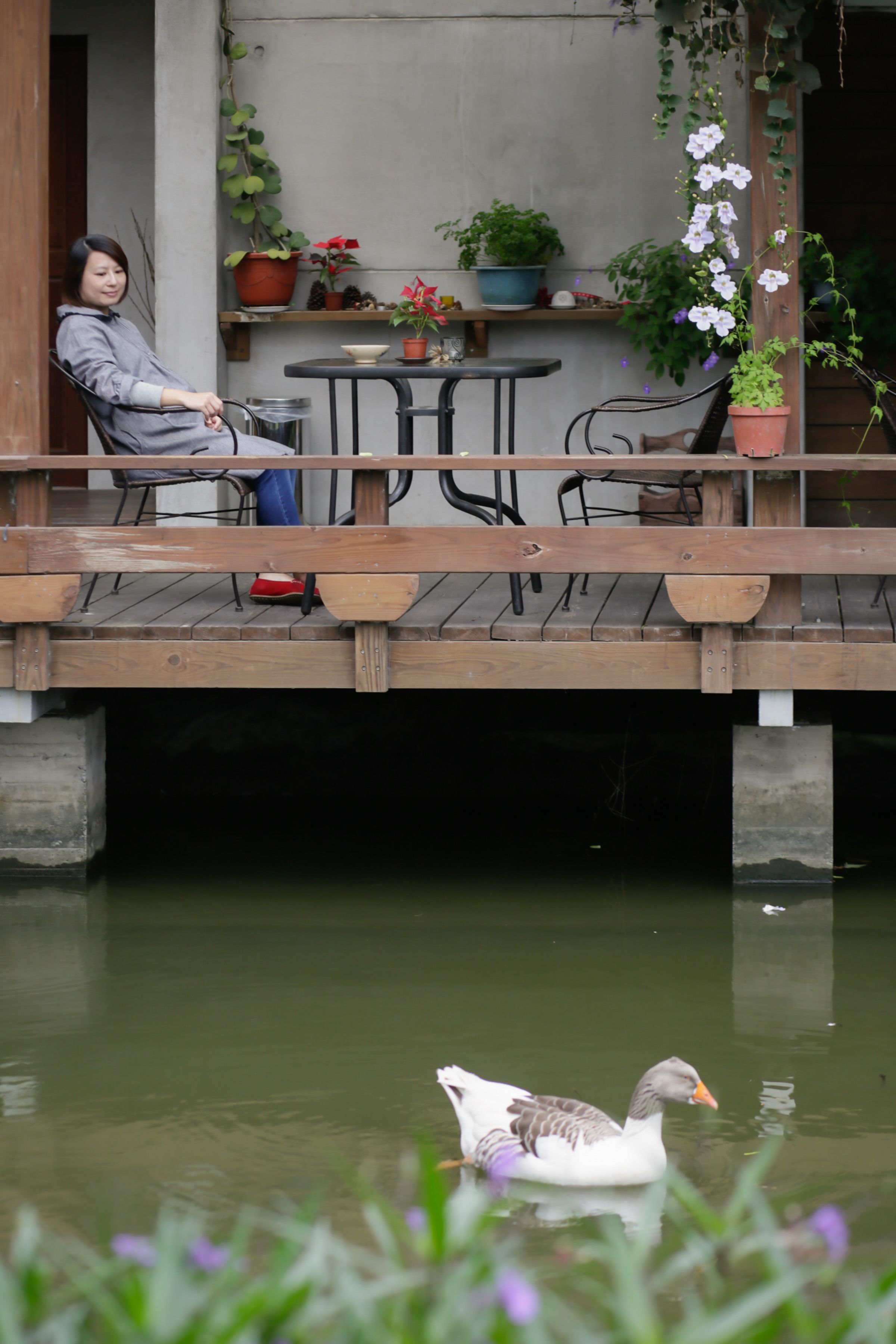 A wooden deck with a table and chairs, overlooking a body of water with a duck swimming.