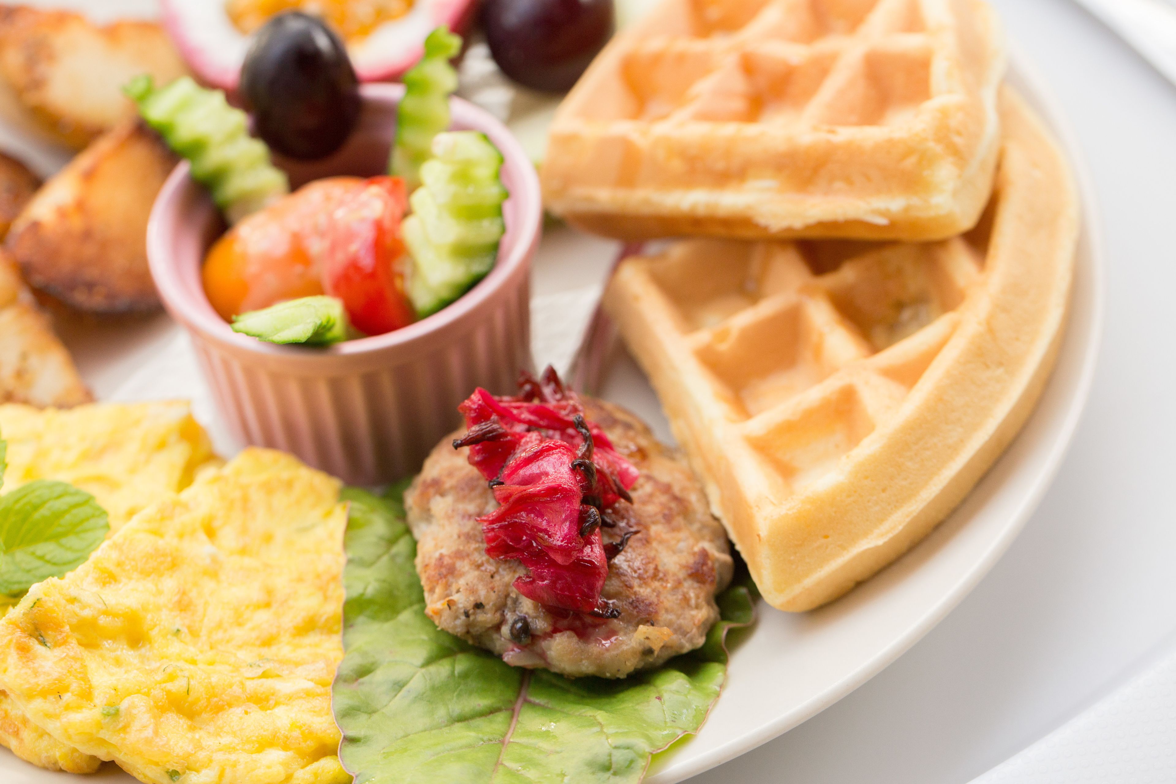 Ein Teller mit verschiedenen Speisen, darunter ein Waffel, eine Fleischpflanzerl, ein Omelett und ein Salat.