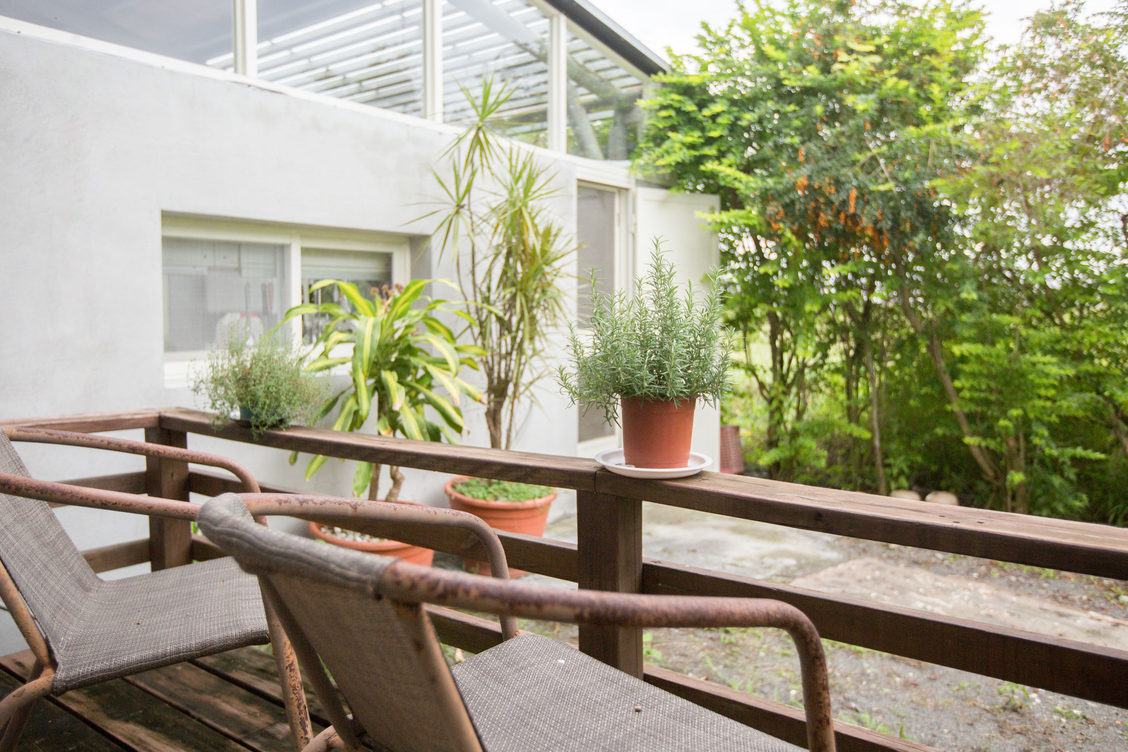 A wooden deck with two wicker chairs, a potted plant, and a view of a garden and building.