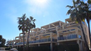 A multi-story building with balconies, surrounded by palm trees and a well-maintained lawn.