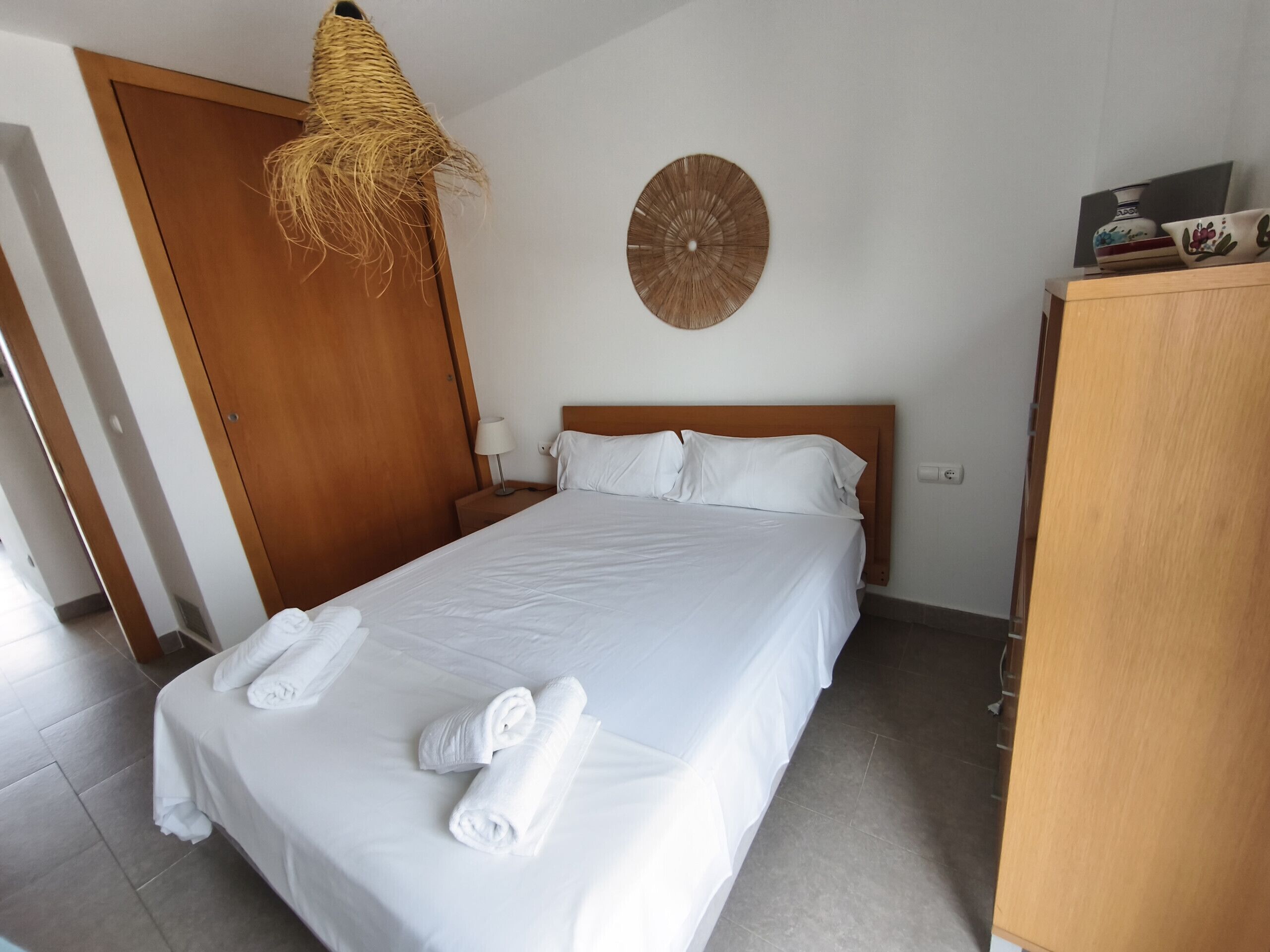 A hotel room with a bed, a wooden wardrobe, a wall clock, and a hanging light fixture.