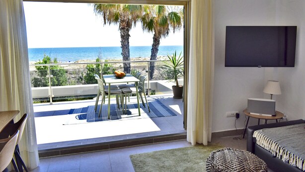 A bedroom with a balcony overlooking the beach, a TV, and a desk with a lamp.