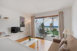 Een moderne woonkamer met een televisie, witte planken, een eettafel en een bank.