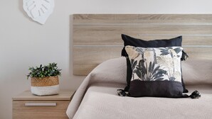 A bedroom with a wooden headboard, a bed with a floral pillow, a nightstand with a plant, and a heart-shaped decoration on the wall. - Charming "La Florida" Apartment with Pool, Balcony, Sea Views & Wi-Fi (Tías)