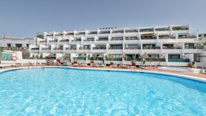 A swimming pool with lounge chairs and umbrellas, surrounded by a multi-story hotel with balconies. - Charming "La Florida" Apartment with Pool, Balcony, Sea Views & Wi-Fi (Tías)
