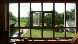 Una habitación con un ventanal grande con vistas a un paisaje rural, una chimenea de ladrillo y una pequeña mesa con un control remoto.