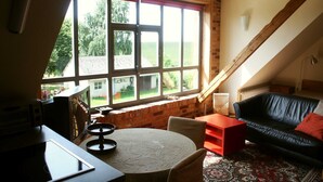 Una habitación acogedora con un ventanal grande, un sofá de cuero negro, una mesita y una mesita auxiliar roja.