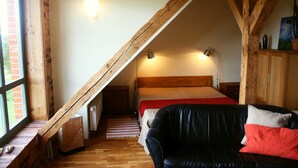 Un dormitorio con techo inclinado, una cama, un sofá de cuero negro, un armario de madera y una ventana con vistas al exterior.