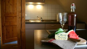 Una encimera de cocina con una botella de vino tinto, una copa, un trozo de queso y una tajada de sandía.