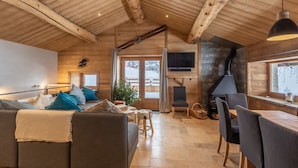 A cozy cabin interior with a wooden ceiling, a fireplace, a TV mounted on the wall, and a dining area with a table and chairs.