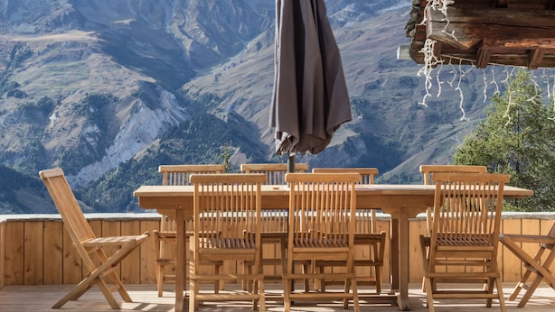 A wooden deck with a table and chairs overlooking a mountainous landscape.