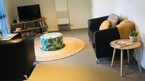 A living room with a black sofa, a round ottoman, a small side table, and a television on a wooden stand. - Tranquil Pet friendly, close to the airport, free NBN and Netflix! (East Albury)