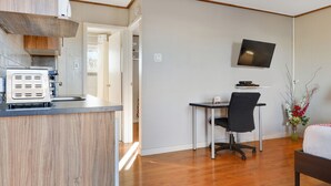 A compact hotel room with a kitchenette, a desk with a chair, a bed, and a TV mounted on the wall.