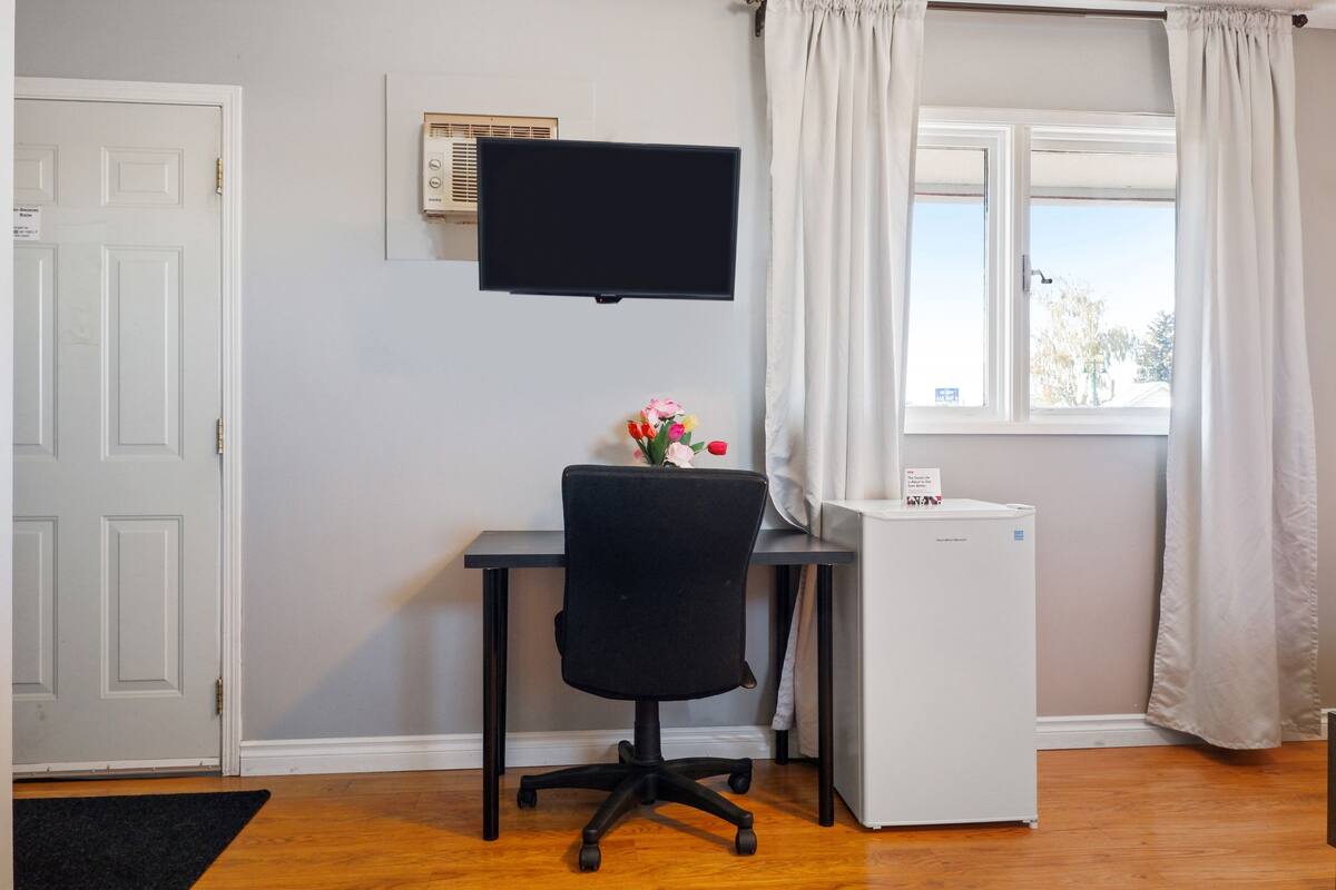 A room with a desk, chair, TV, and a small white appliance.