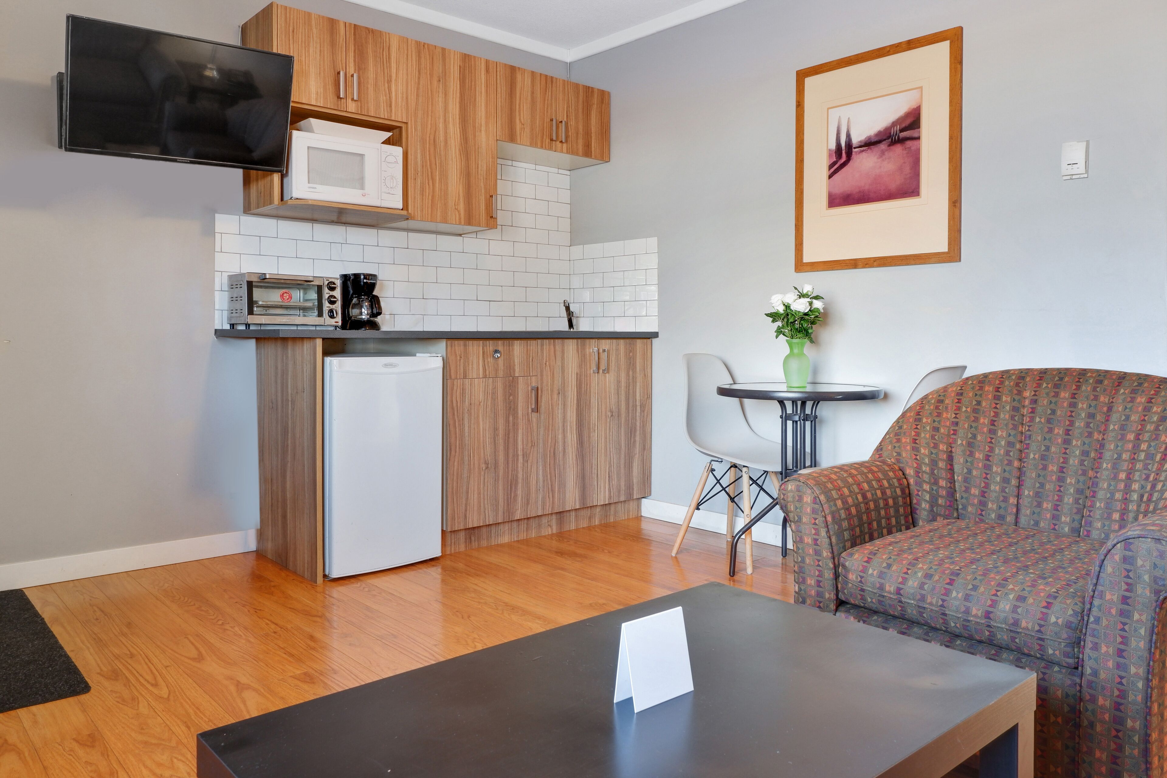 Un espacio habitable pequeño con kitchenette, un sofá, una mesita de centro y un cuadro en la pared.