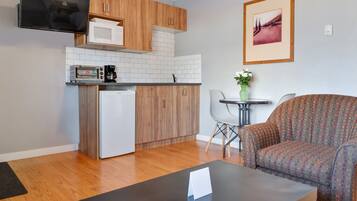 Un espacio habitable pequeño con kitchenette, un sofá, una mesita de centro y un cuadro en la pared.