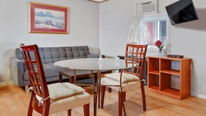 A dining area with a round glass table, four wooden chairs, a grey sofa, a wooden sideboard, and a mounted TV.