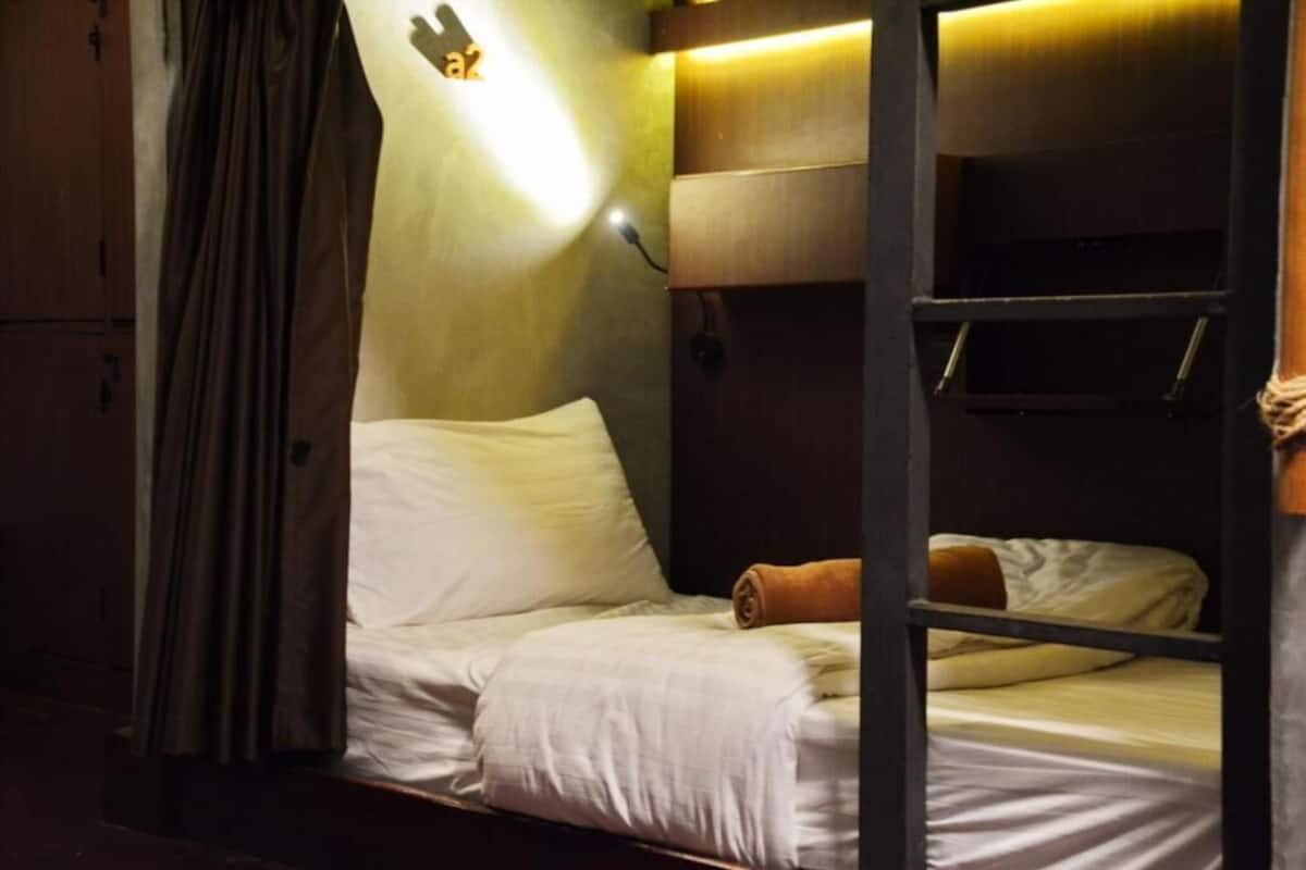 A bunk bed room with a headboard, a curtain, and a wall-mounted light fixture.