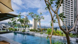 A rooftop infinity pool with a view of a cityscape, surrounded by greenery and modern buildings. - LIVIE Da Nang Style (Da Nang)