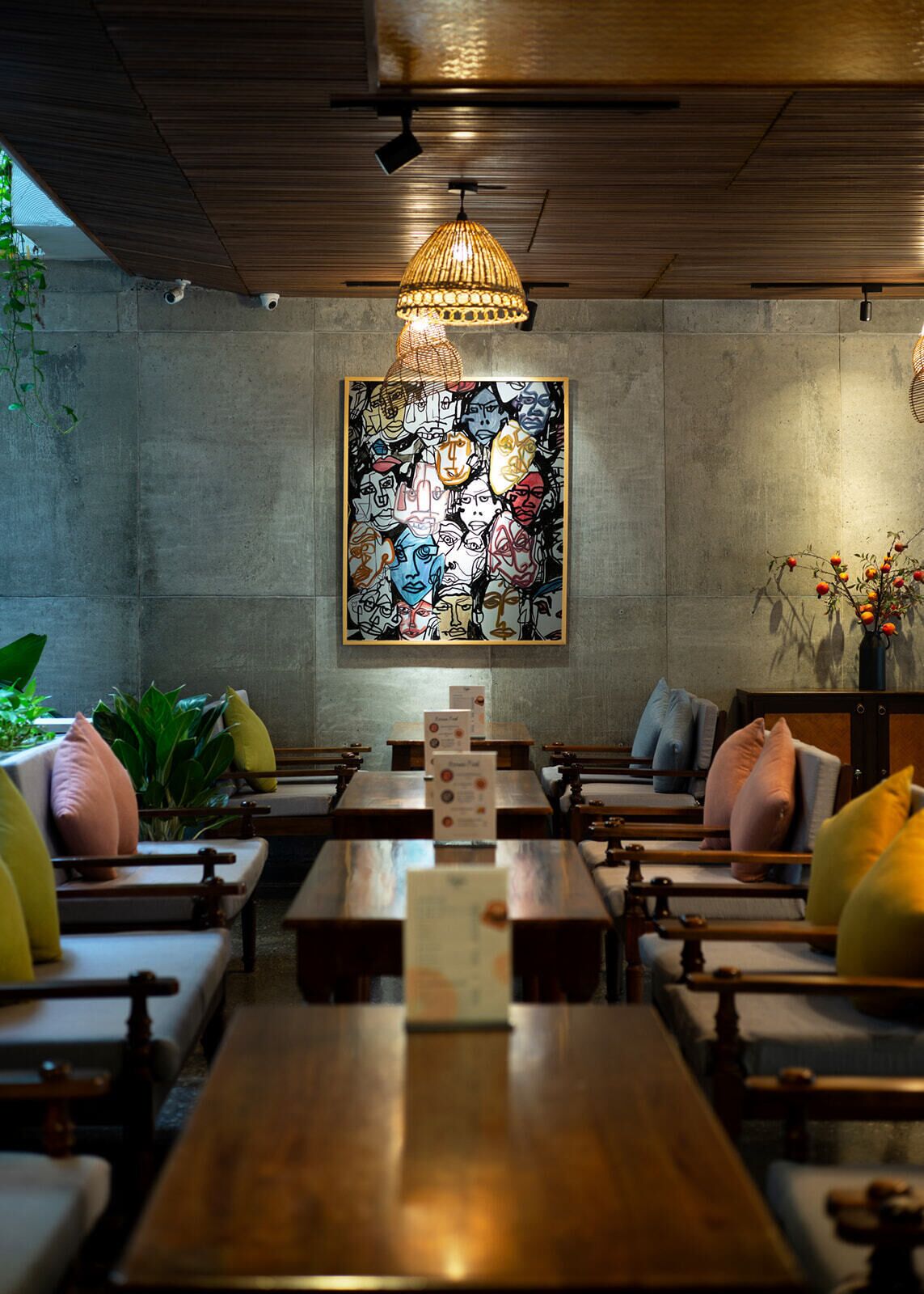 Un restaurante con mesas y sillas de madera, un gran cuadro abstracto en la pared y una lámpara colgante.