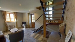 A spacious living room with a wooden staircase, a television, and a dining area with a table and chairs. - "Les Vieux Poiriers" (near Taize, Cluny ..) in Bonnay 71460 (Cluniac site) (Bonnay)