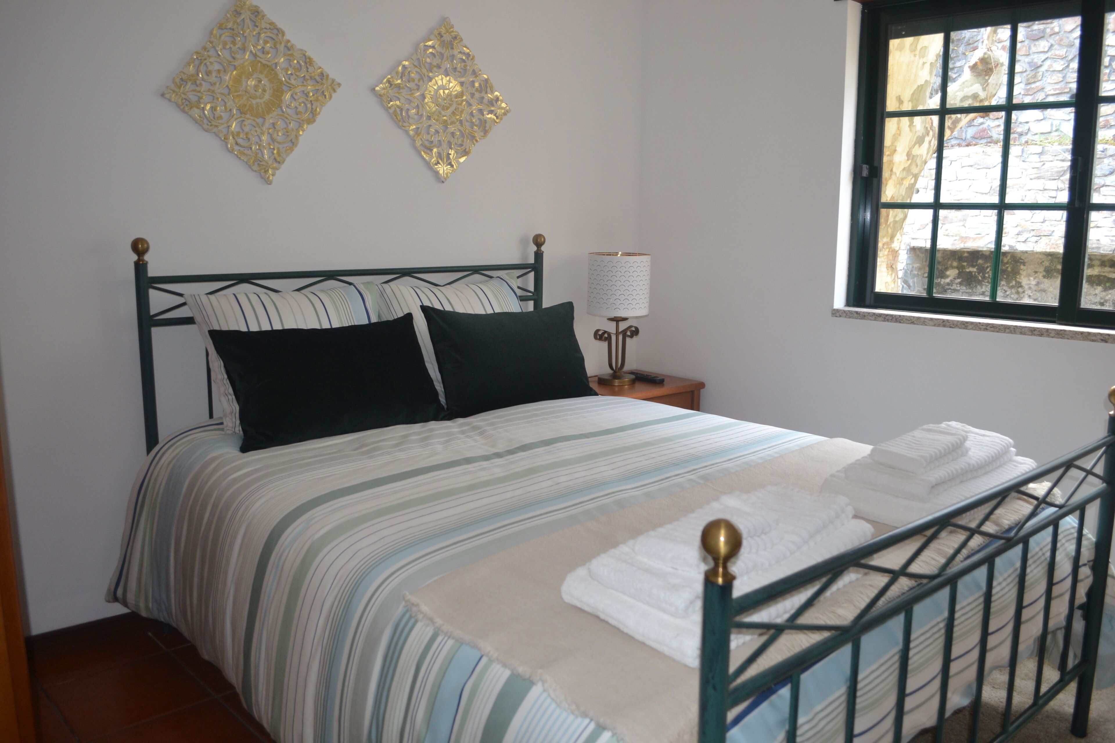 Een net opgemaakt bed met gestreept beddengoed, een bedlampje en decoratieve muurkunst.