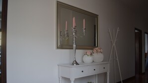 Una consola blanca con un espejo encima, un candelabro con velas rosas y dos jarrones con flores.