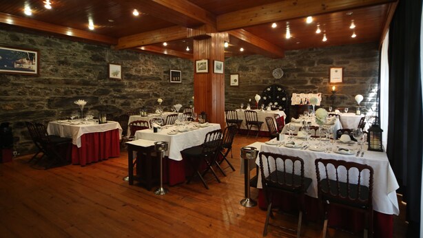 Un comedor con mesas y sillas de madera, paredes de piedra y cuadros enmarcados.
